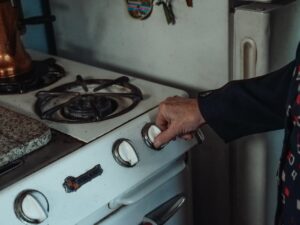 Close-up of a hand turning a knob on a retro gas stove in a home kitchen setting.
