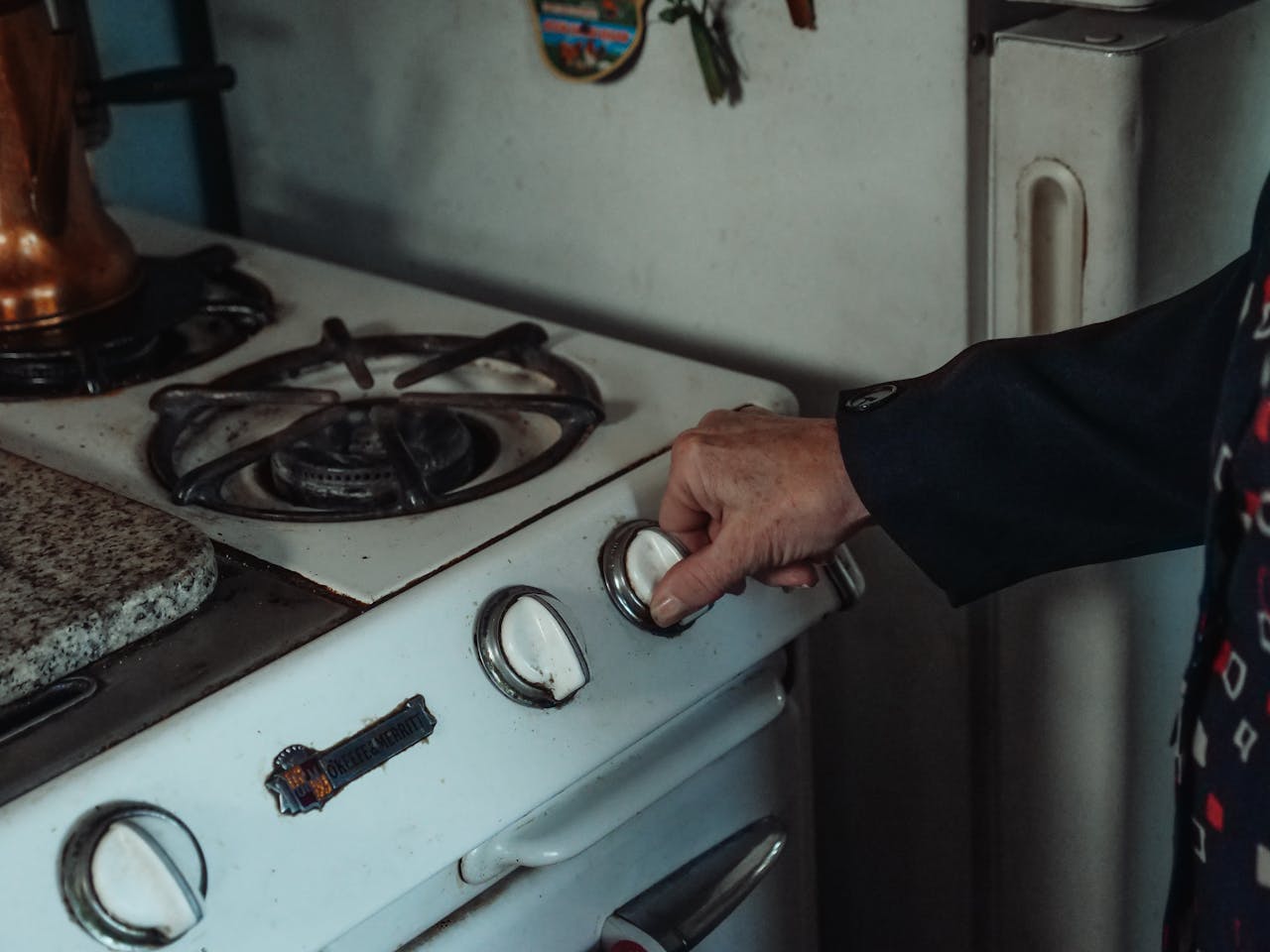 Close-up of a hand turning a knob on a retro gas stove in a home kitchen setting.